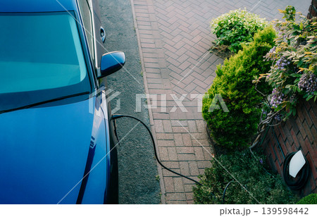 Top view electric car plugged into a charging station while parked in home. Residential EV Charging Station. Home EV Charging. Sustainable Power of a Wall-Mounted Charger. Future of Clean Transport. Top view electric car plugged into a charging station while parked in home. Residential EV Charging Station. Home EV Charging. Sustainable Power of a Wall-Mounted Charger. Future of Clean Transport. 139598442