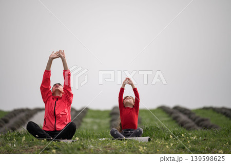 Yoga practice in a serene field with vibrant greenery and soft sunlight illuminating a peaceful connection between a parent and child at dawn 139598625