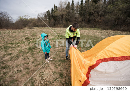 Camping adventure unfolds as a father teaches his daughter the art of tent setup amidst a serene landscape under overcast skies in early spring Camping adventure unfolds as a father teaches his daughter the art of tent setup amidst a serene landscape under overcast skies in early spring 139598660
