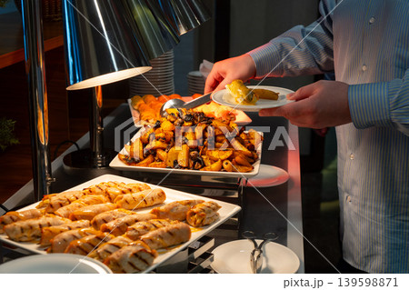Person serving hot dishes at a hotel buffet with tongs Person serving hot dishes at a hotel buffet with tongs 139598871