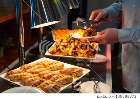 Person serving hot buffet food under warming lamps Person serving hot buffet food under warming lamps 139598872