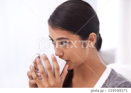 Coffee, drinking and Indian woman on sofa for relax, comfortable and calm in home for wellness. Apartment, morning and person with mug on couch for hot beverage, tea and caffeine drink in living room Coffee, drinking and Indian woman on sofa for relax, comfortable and calm in home for wellness. Apartment, morning and person with mug on couch for hot beverage, tea and caffeine drink in living room 139599371