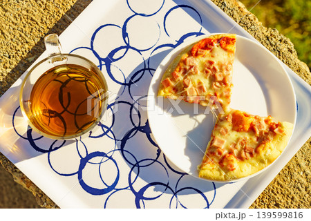 Tea mug and pizza slices on plate, outdoors Tea mug and pizza slices on plate, outdoors 139599816