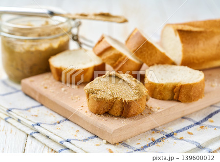 Creamy pate curls on a slice of baguette bread on a white table, selective focus. 139600012