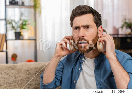 Man in headphones suddenly takes them off looking surprised reacting to strange unexpected sound Man in headphones suddenly takes them off looking surprised reacting to strange unexpected sound 139600400