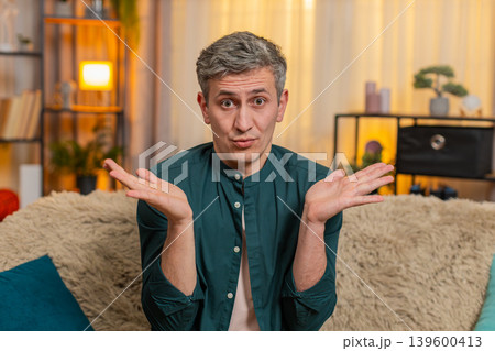 Young man lifts hands in air and looks confused reacting to unexpected situation or sudden question 139600413