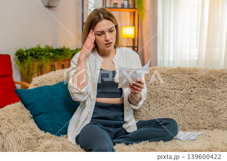 Adult woman reacting to financial stress at home reading utility bills sad worried expression stress Adult woman reacting to financial stress at home reading utility bills sad worried expression stress 139600422
