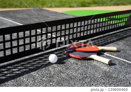 Table tennis rackets close-up. Ping pong rackets and ball on a public table in city park Table tennis rackets close-up. Ping pong rackets and ball on a public table in city park 139600460