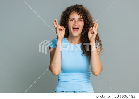 Young woman smiling crossing fingers hoping good luck wish positive optimistic anticipation gesture 139600483