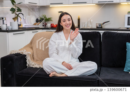 Young woman waves hello smiles greeting camera hand gesture cheerful welcome sign positive mood warm Young woman waves hello smiles greeting camera hand gesture cheerful welcome sign positive mood warm 139600671