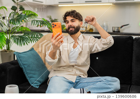 Indian man smartphone video call smiling showing apartment keys to family celebrating new life start Indian man smartphone video call smiling showing apartment keys to family celebrating new life start 139600686