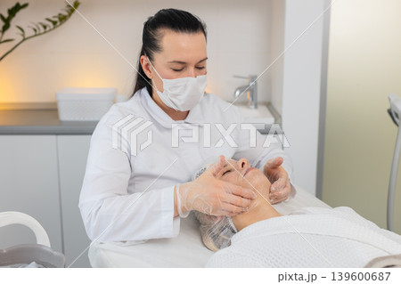Cosmetology clinic facial peeling beautician rubbing moisturizing cream on middle aged woman skin Cosmetology clinic facial peeling beautician rubbing moisturizing cream on middle aged woman skin 139600687