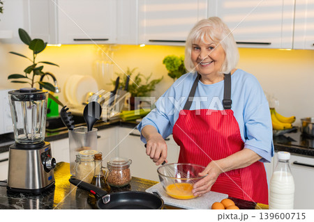 Senior old woman whisking eggs for healthy omelet breakfast in home kitchen diet fit cooking routine 139600715