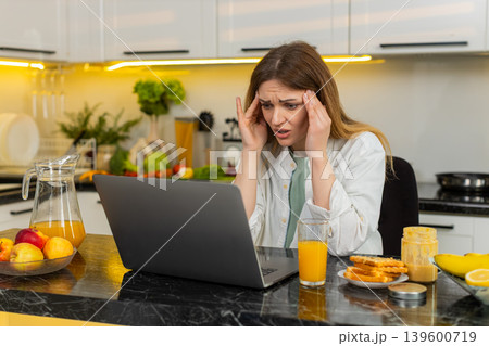 Middle-aged woman shocked by bad news on laptop in kitchen feeling stress after failure loss online Middle-aged woman shocked by bad news on laptop in kitchen feeling stress after failure loss online 139600719