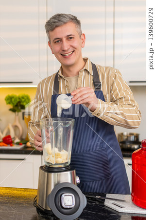 Middle-aged man pouring protein powder into blender for healthy shake meal prep in kitchen at home Middle-aged man pouring protein powder into blender for healthy shake meal prep in kitchen at home 139600729