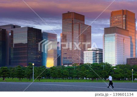Tokyo, Japan - Oct 1 2024, panoramic view of the Chiyoda district's skyscrapers, with a parking lot with people walking in the foreground, and colorful clouds at sunset.Tokyo, Japan Tokyo, Japan - Oct 1 2024, panoramic view of the Chiyoda district's skyscrapers, with a parking lot with people walking in the foreground, and colorful clouds at sunset.Tokyo, Japan 139601134