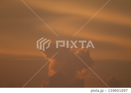 Dramatic towering cloud illuminated by warm sunset light against a deep orange sky, creating a moody atmospheric nature background with soft glowing tones. Dramatic towering cloud illuminated by warm sunset light against a deep orange sky, creating a moody atmospheric nature background with soft glowing tones. 139601897