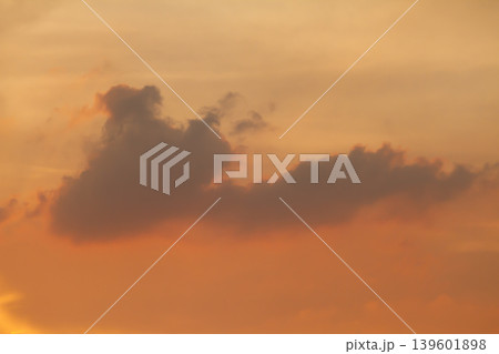 Atmospheric sunset scene with dark floating clouds over a glowing orange sky, creating a dramatic and peaceful natural background with soft evening light. 139601898