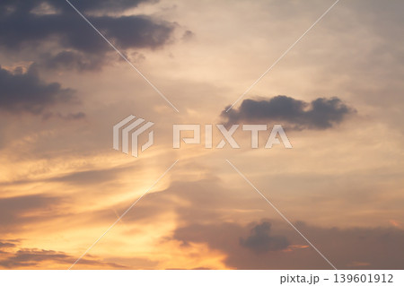 Gentle pastel clouds stretch across a glowing sunset sky with warm light and subtle atmospheric textures, creating a serene natural background at twilight. 139601912