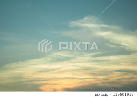 Delicate pastel clouds floating across a serene blue sky with warm evening tones, creating a peaceful atmospheric background for nature and design projects. 139601919