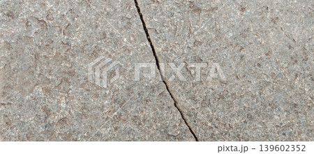 A close-up image of a rough textured stone or concrete surface with a natural crack running down the middle. 139602352