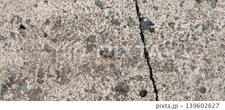 Close up of an asphalt concrete surface with natural cracks and small stone details scattered throughout the surface. 139602627