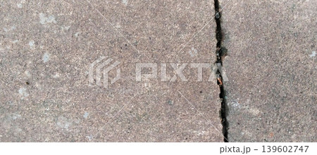 Close-up photo of a paving or concrete surface with natural vertical cracks and a rough, gray-brown texture. Close-up photo of a paving or concrete surface with natural vertical cracks and a rough, gray-brown texture. 139602747