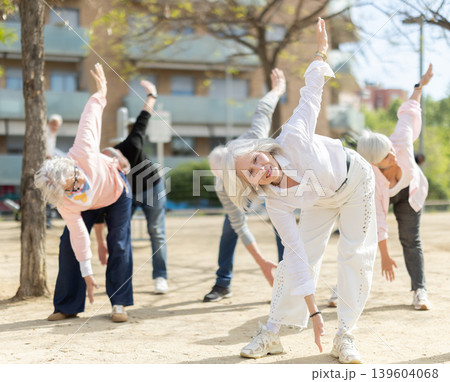 Group of elderly people perform arm swinging exercise physical activity outdoors. 139604068