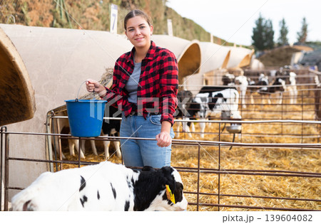 Caring young female farmer in plaid shirt giving milk to calves in plastic calf hutch on farm in countryside in autumn 139604082