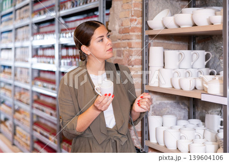Positive woman chooses mug or cup in pottery and ceramics shop Positive woman chooses mug or cup in pottery and ceramics shop 139604106
