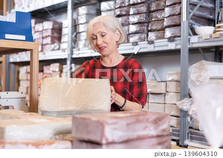 Elderly woman carefully chooses briquettes with white clay in specialized store Elderly woman carefully chooses briquettes with white clay in specialized store 139604310