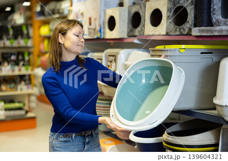 Female cat owner choosing plastic litter tray in pet shop 139604321