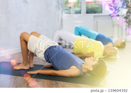 Mother, grandmother and adolescence son do half bridge Setu Bandha Sarvangasana, glute bridge pose Mother, grandmother and adolescence son do half bridge Setu Bandha Sarvangasana, glute bridge pose 139604392