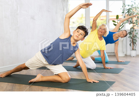 Grandmother, mother and teen son do deadbolt pose, parighasana in gym Grandmother, mother and teen son do deadbolt pose, parighasana in gym 139604405