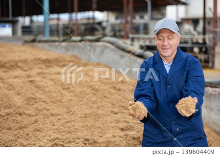Middle-aged man farmer checking beer oilcake in fodder storage 139604409