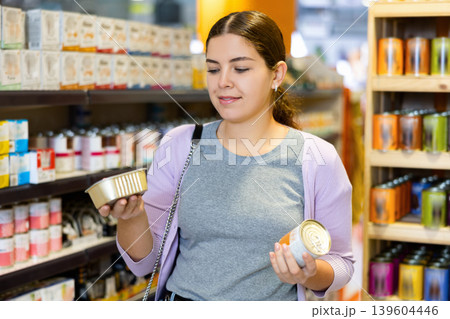 Young female customer picking out canned pet food in pet store Young female customer picking out canned pet food in pet store 139604446