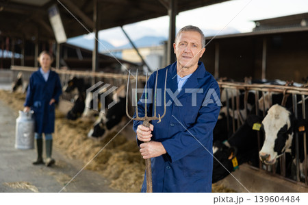 Male farmer with pitchfork standing in cowshed Male farmer with pitchfork standing in cowshed 139604484