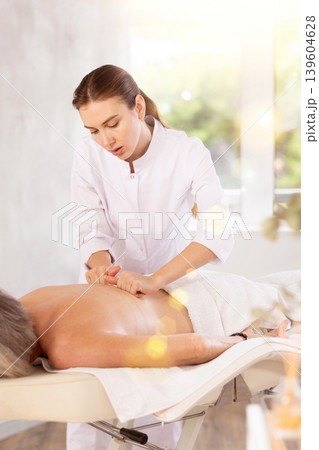 Professional young masseuse doing back massage to elderly woman Professional young masseuse doing back massage to elderly woman 139604628