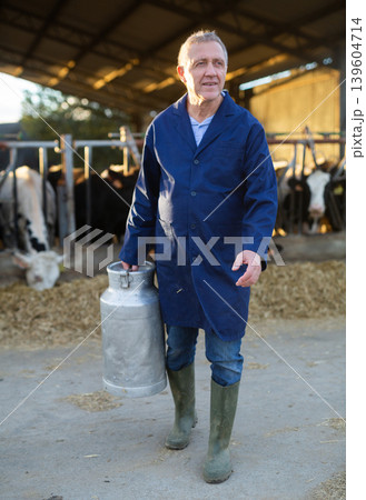 Man farmer carrying milk can in cowhouse Man farmer carrying milk can in cowhouse 139604714
