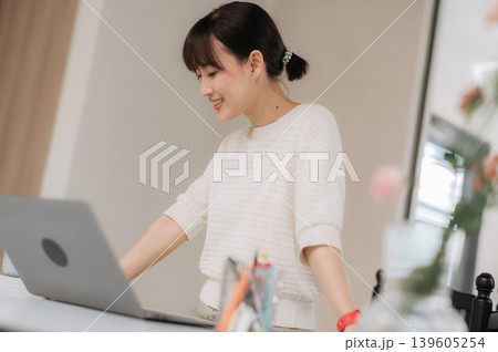 Happy smiling asian woman using modern technology computer working standing at bright desk inside home office room Happy smiling asian woman using modern technology computer working standing at bright desk inside home office room 139605254