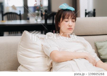 Exhausted asian woman resting on sofa with ice pack suffering from headache after using technology feeling sad and unwell Exhausted asian woman resting on sofa with ice pack suffering from headache after using technology feeling sad and unwell 139605268