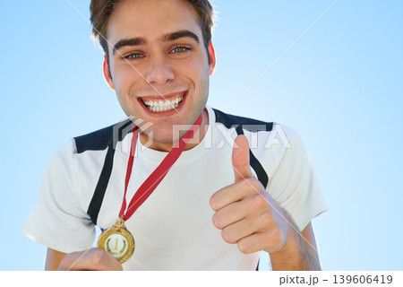 Winner, man and thumbs up with medal for sports achievement, success and yes in competition. Happy portrait of runner or athlete with like, prize or good job hands, emoji and gold award on a blue sky Winner, man and thumbs up with medal for sports achievement, success and yes in competition. Happy portrait of runner or athlete with like, prize or good job hands, emoji and gold award on a blue sky 139606419