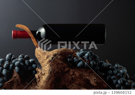 Unopened bottle of red wine, blue grapes, and weathered snag. 139608152