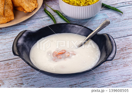 Bowl of creamy shrimp soup with a spoon on a rustic light blue wooden table with fresh chili peppers. 139608505