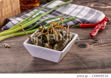 Pickled caper berries in a bowl with fresh ingredients on a rustic wooden table. Pickled caper berries in a bowl with fresh ingredients on a rustic wooden table. 139608516