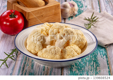 Fresh cauliflower florets in a bowl with tomato, garlic, and rosemary on a rustic wooden table Fresh cauliflower florets in a bowl with tomato, garlic, and rosemary on a rustic wooden table 139608524