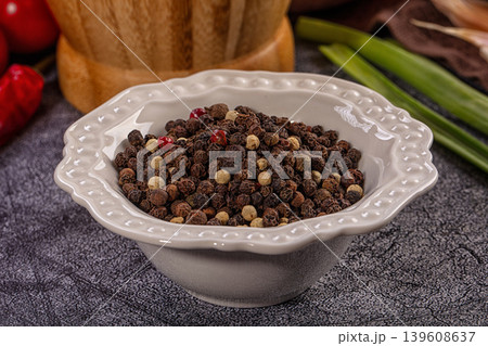 Assorted whole peppercorns in decorative white bowl, red chili and wooden spice mill background Assorted whole peppercorns in decorative white bowl, red chili and wooden spice mill background 139608637