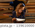 An overburdened woman studying in a library for final exams	 139610000