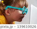 Small child with glasses exposed to blue light from a computer, introducing concepts such as the risk of developing eye diseases from accessing electronic devices at an early age. 139610026