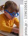 Little girl with blue glasses staring at a computer screen introducing concepts such as effects of screen time on an eye health. 139610041